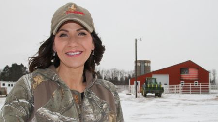 Kristi Noem in a grey top and cap poses in front of an office in snowy condition.
